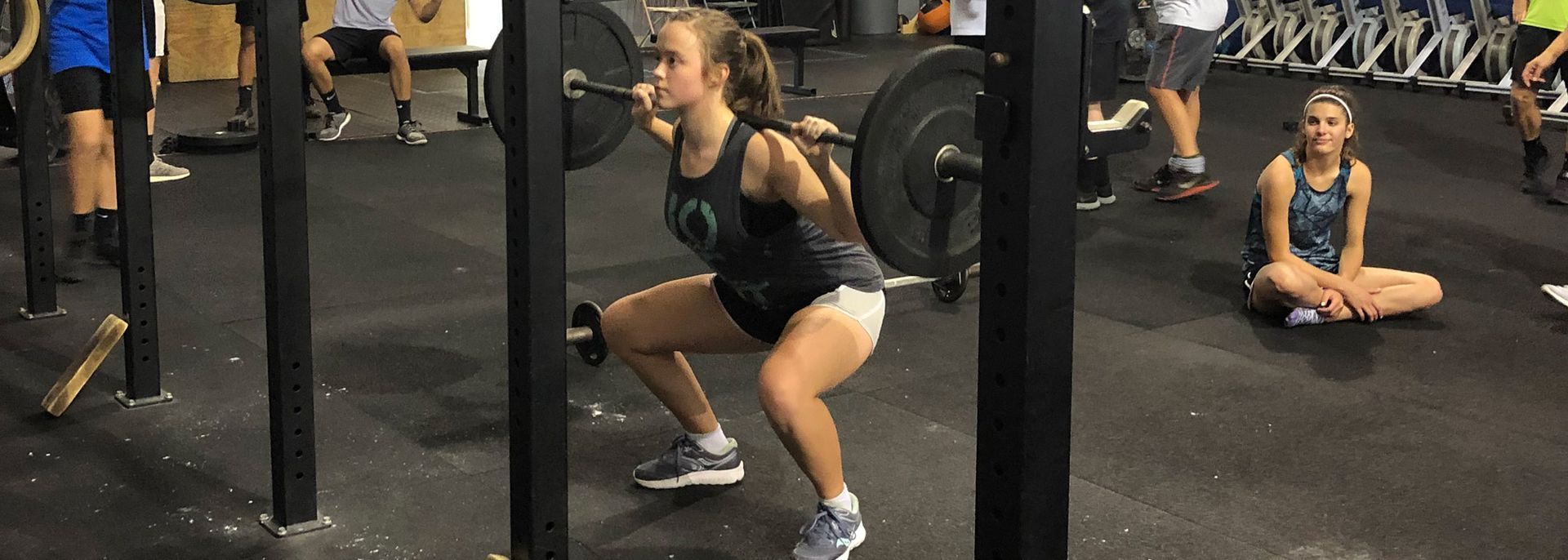 A woman is squatting with a barbell in a gym.
