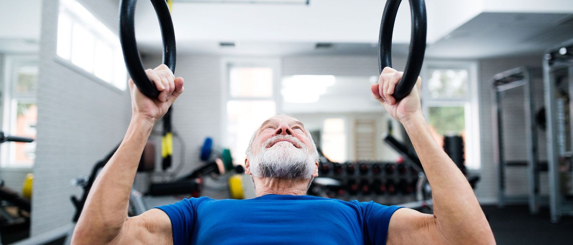 An older man is hanging from gymnastic rings at CrossFit Garage gym in Woodstock, GA