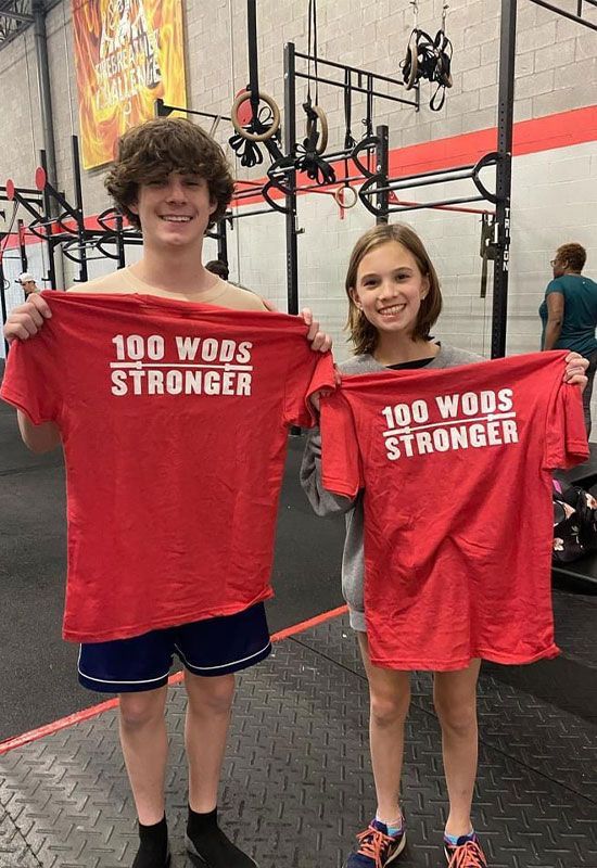 A boy and a girl are holding red shirts that say `` 100 wods stronger ''.