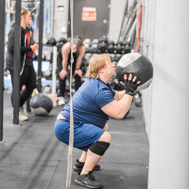 A woman is squatting down while holding a medicine ball in a gym.