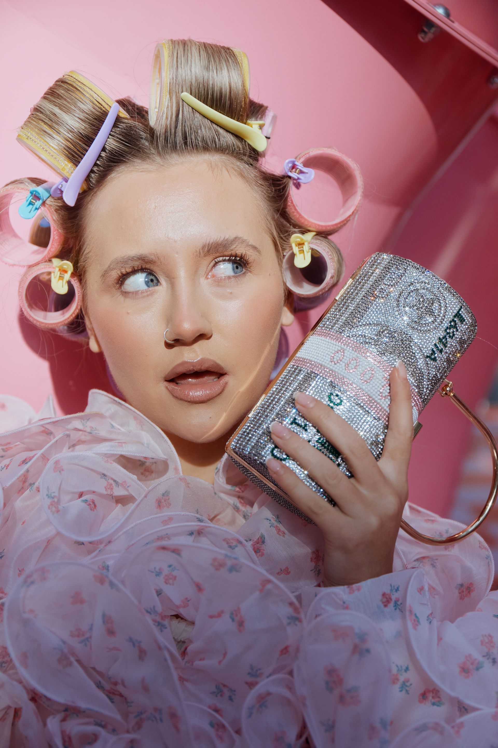 A woman with curlers in her hair is sitting on a bench wearing sunglasses and a fur coat.