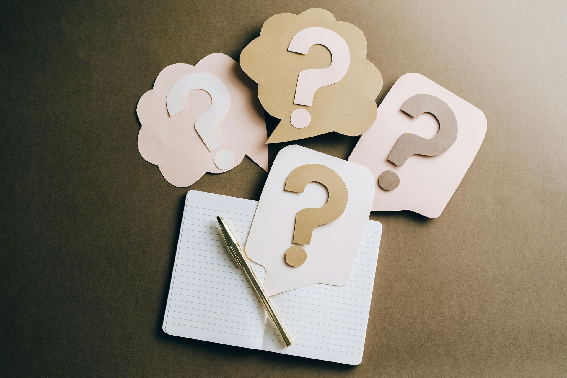 White question-mark cards fanned over a notepad with a pen on a dark background