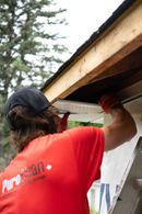 Worker in a red shirt installing trim under a roof eave outdoors
