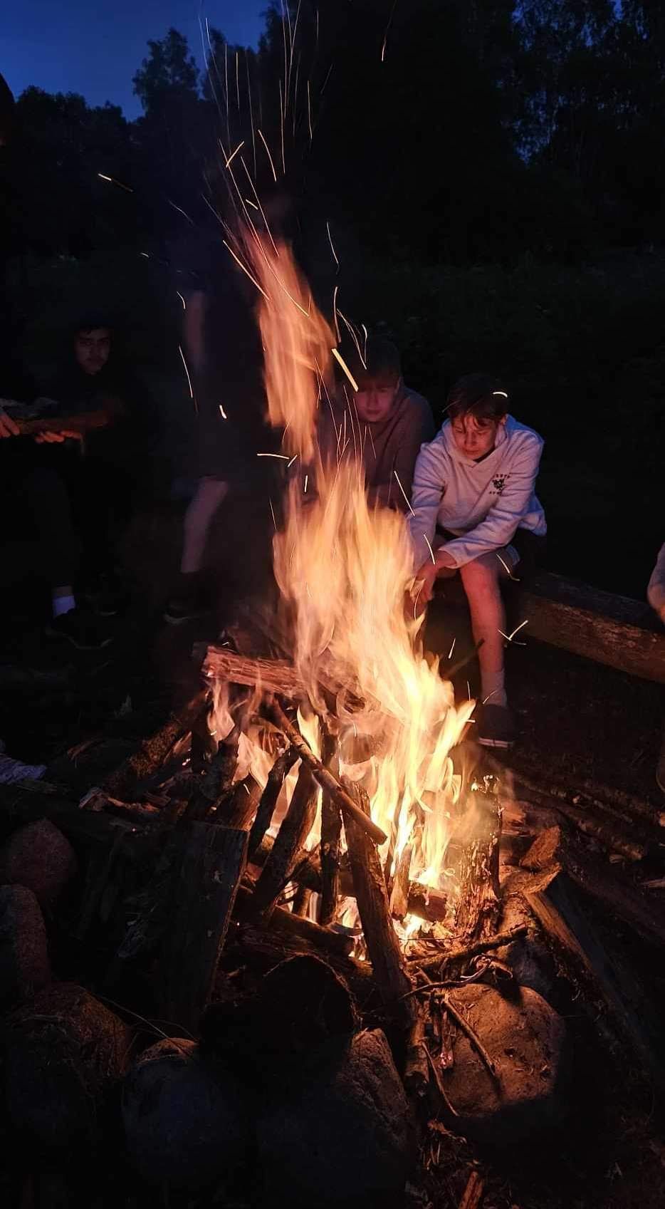 Grupė žmonių naktį sėdi prie laužo.