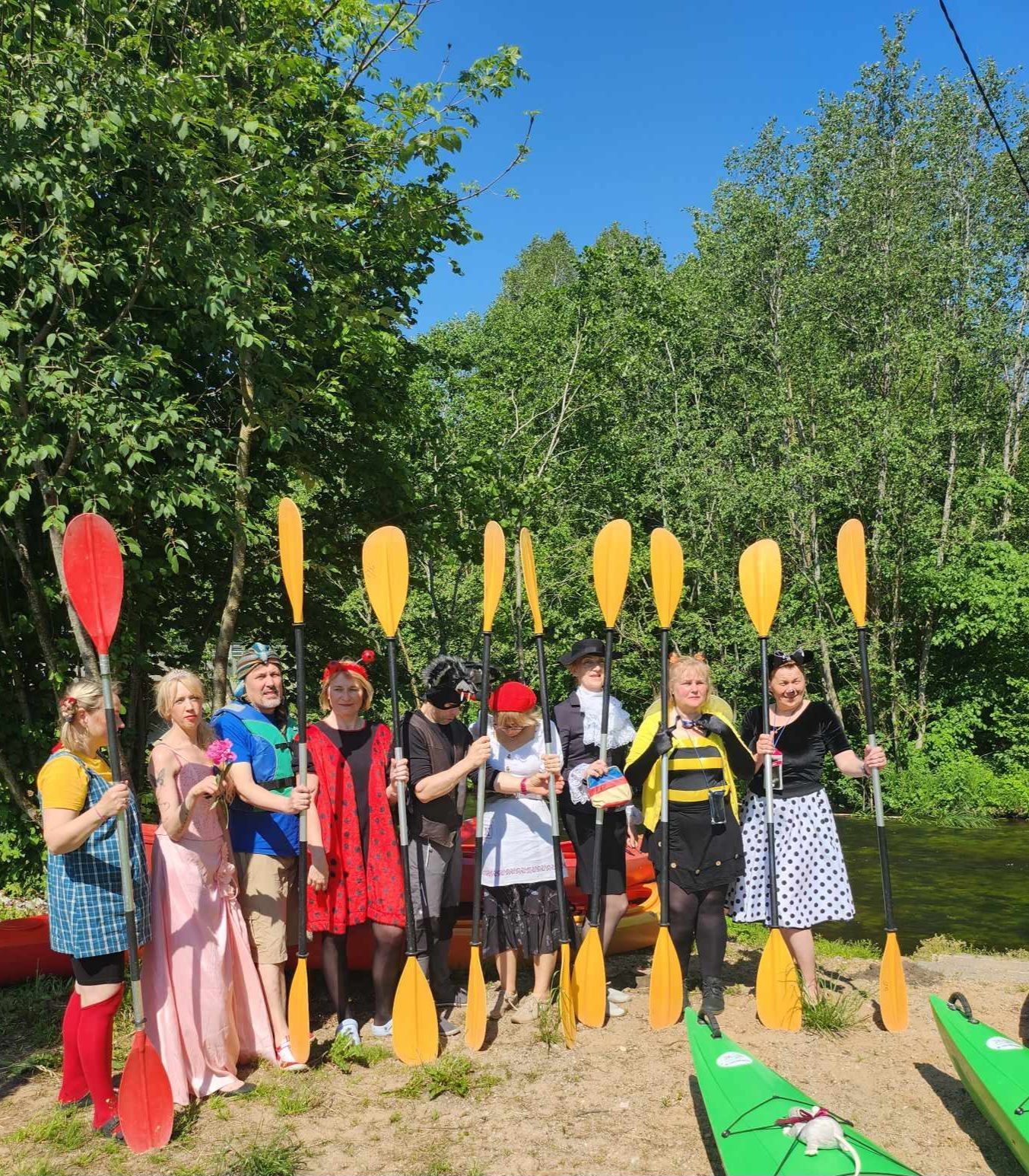 Grupelė žmonių, stovi prie baidarių, laikančių irklus
