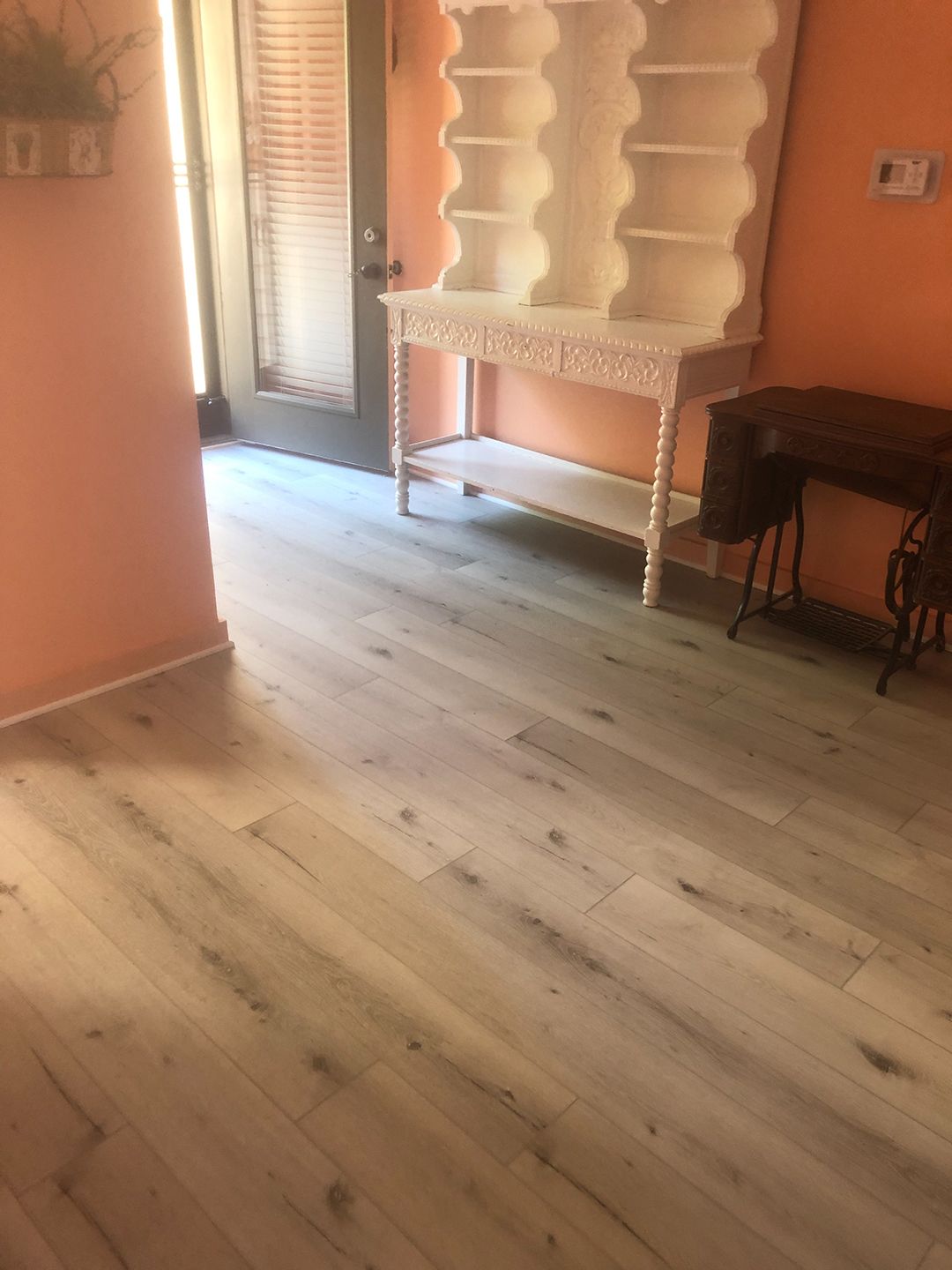 A room with hardwood floors , a desk , shelves and a door.