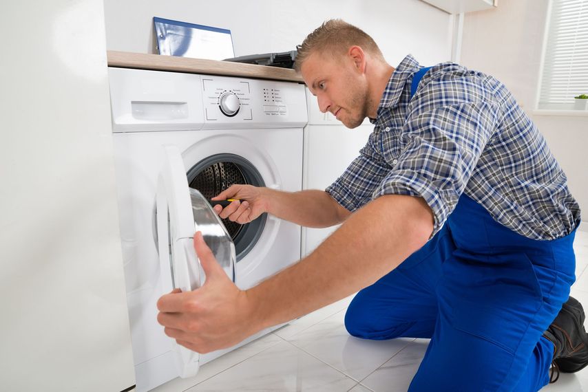 A man is fixing a washer and dryer in a laundry room.