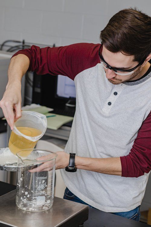 A man is pouring liquid into a beaker in a laboratory.