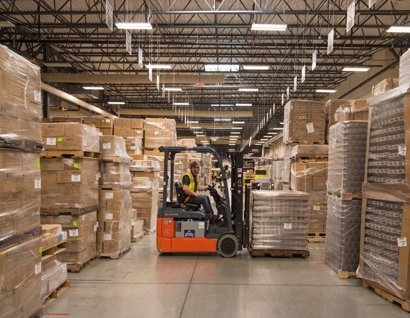 A man is driving a forklift in a warehouse filled with lots of boxes.