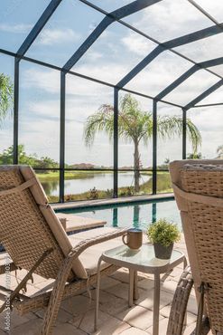 Two beige lounge chairs face a pool and lake view, with a screened enclosure.
