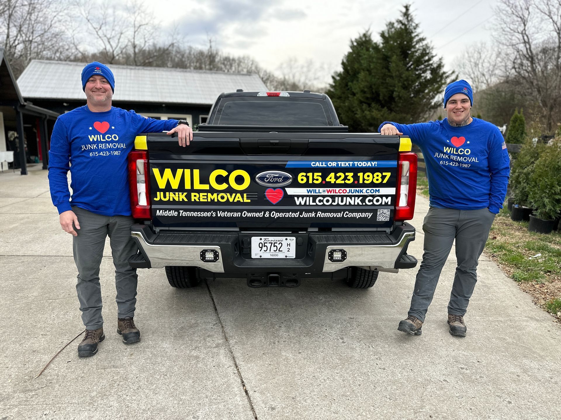 Two men are standing next to a truck that says wilco junk removal.