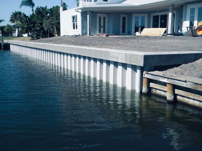Waterfront seawall next to a house under construction; white vertical panels, concrete cap, dark water.