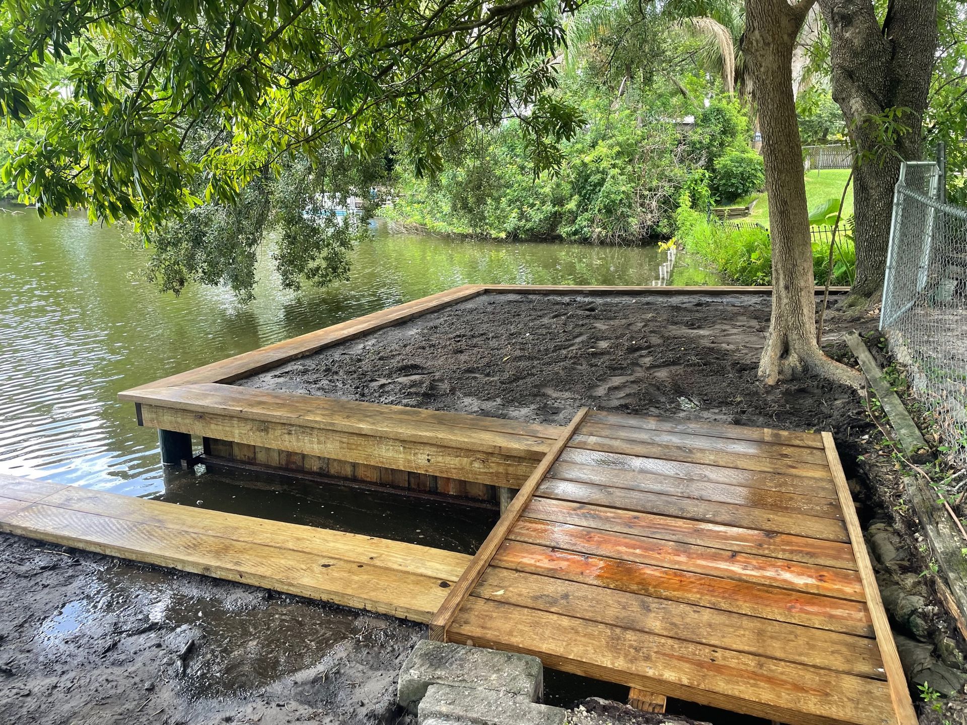 Wooden dock extension under construction next to a body of water and trees.