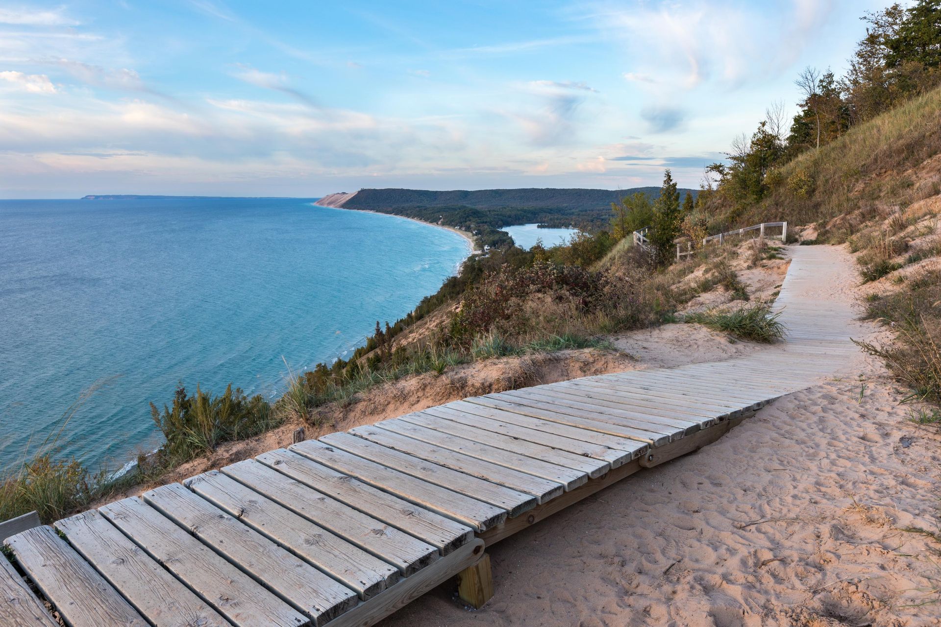 Wooden boardwalk path overlooking blue lake and dunes on a sunny day.