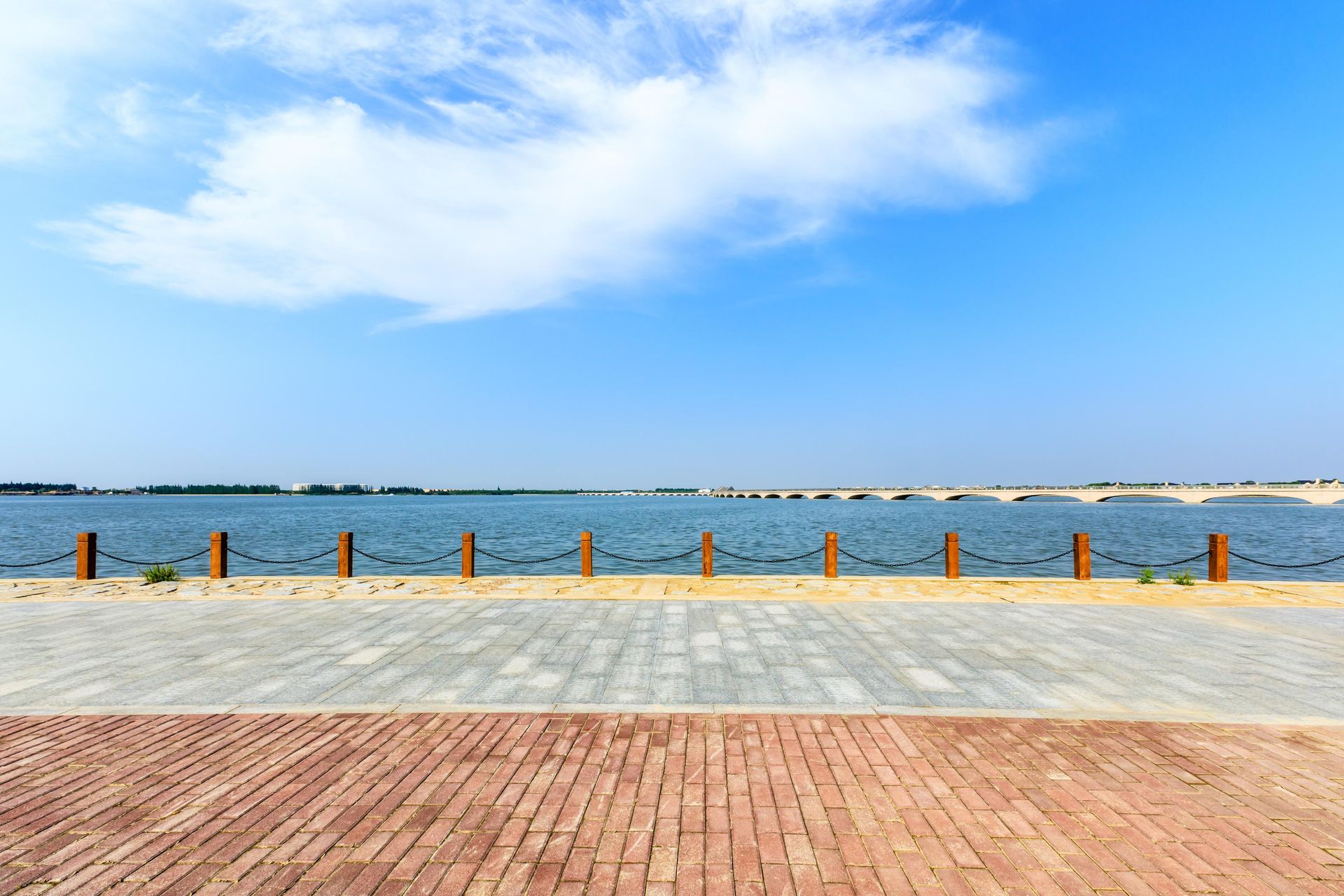 Brick and stone walkway alongside a calm blue lake, with a cloudy sky in the background.