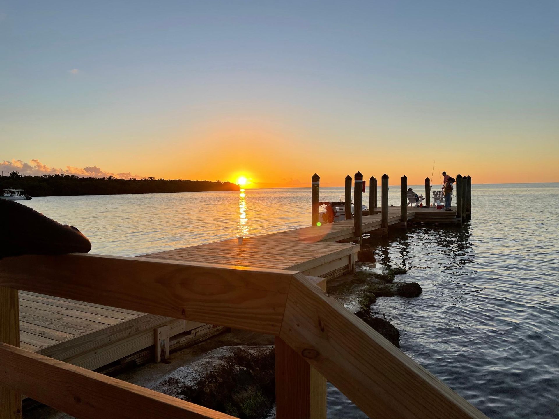 Sunset over water with dock. Bright orange sun, wooden dock, calm water.