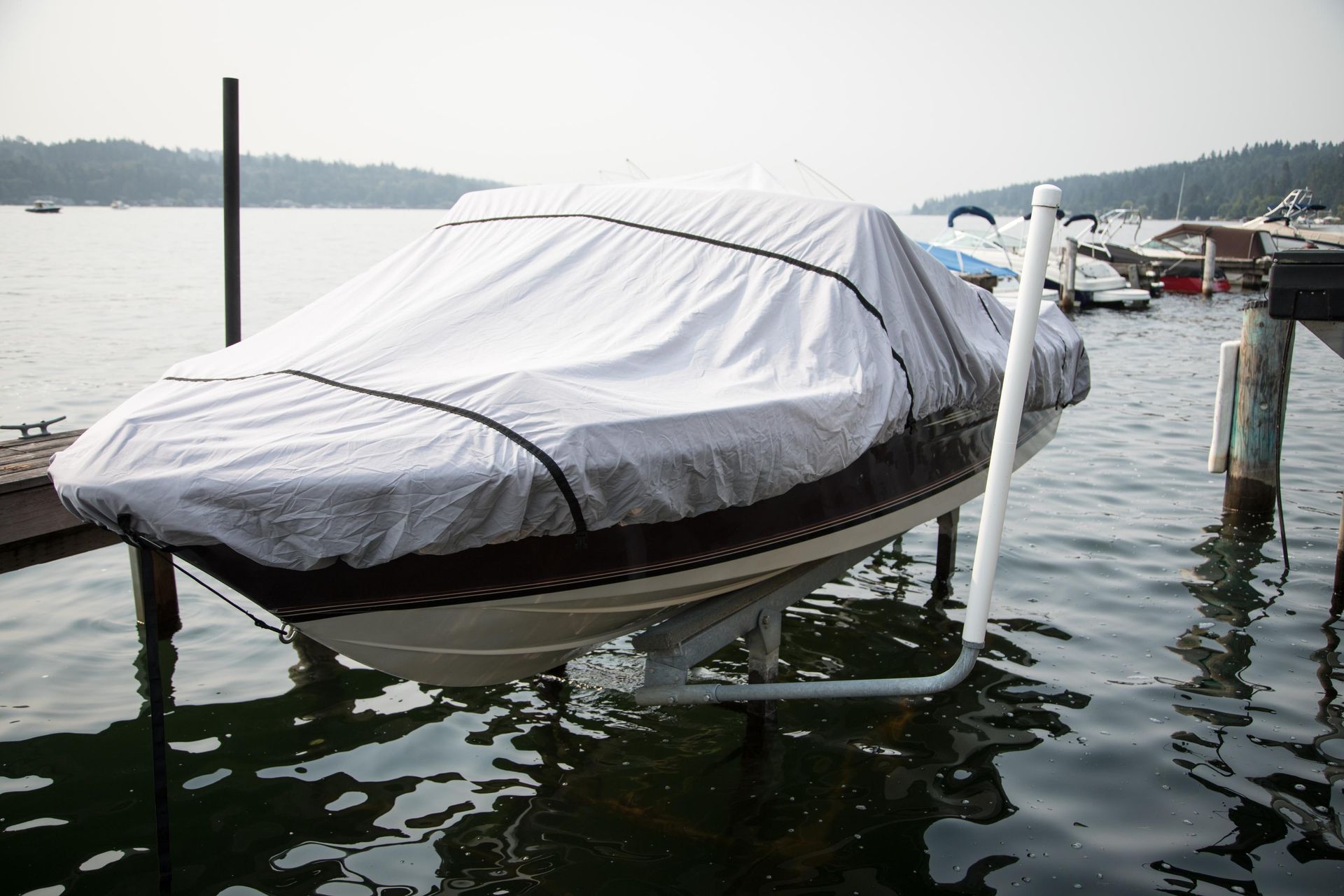 Boat covered with white tarp on a lift in water near a dock, overcast sky.