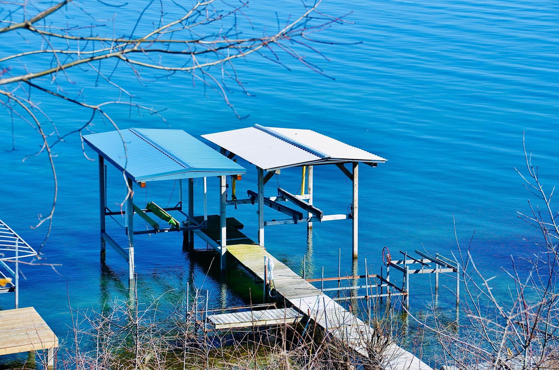 Dock with two boat lifts and blue and white metal roofs extending into blue water.