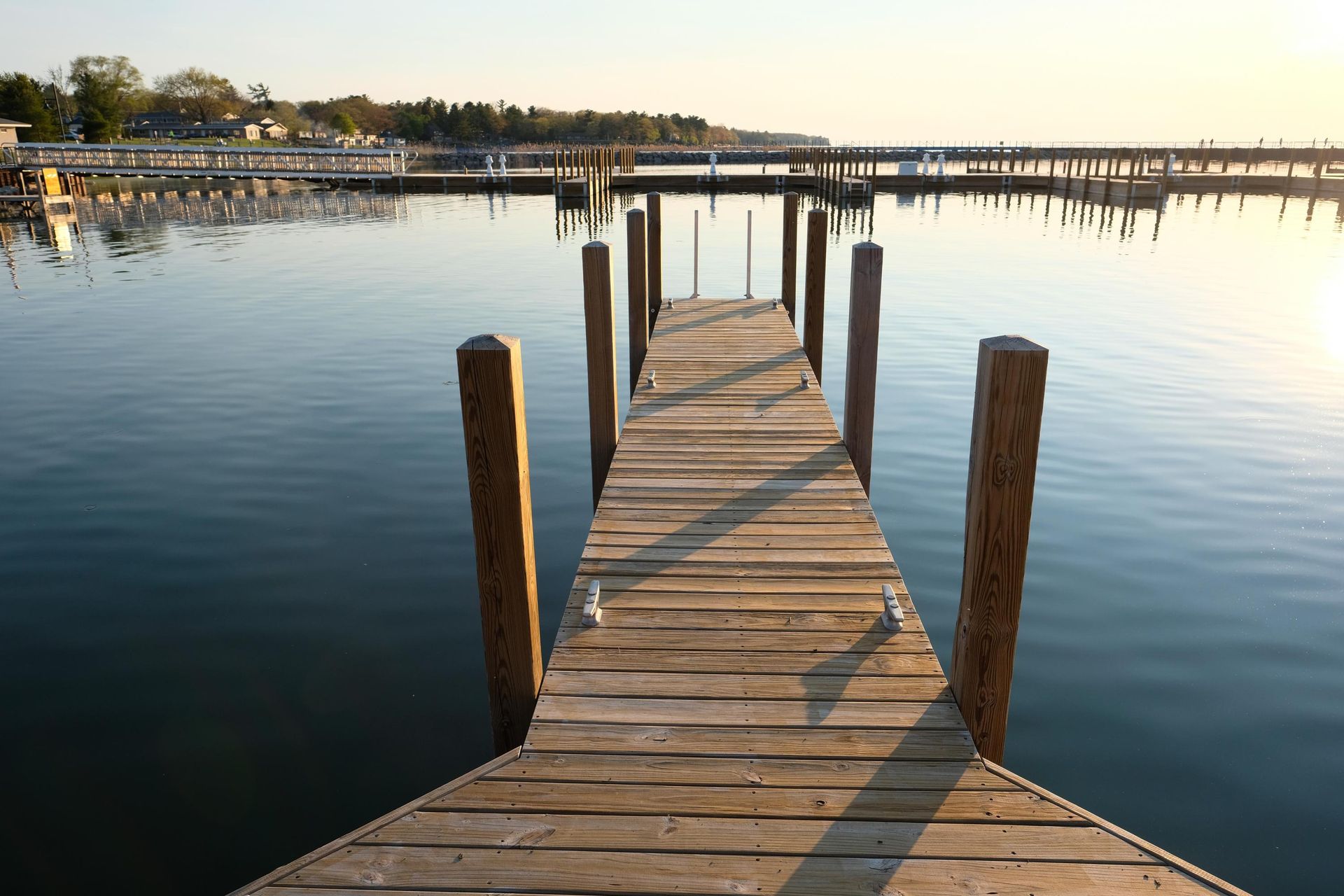 Wooden dock extending into calm water, with other docks and shoreline in the background at sunset.