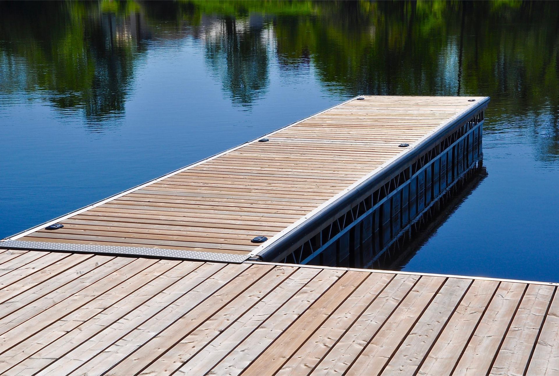 Wooden dock extending into calm blue water with reflections of trees.