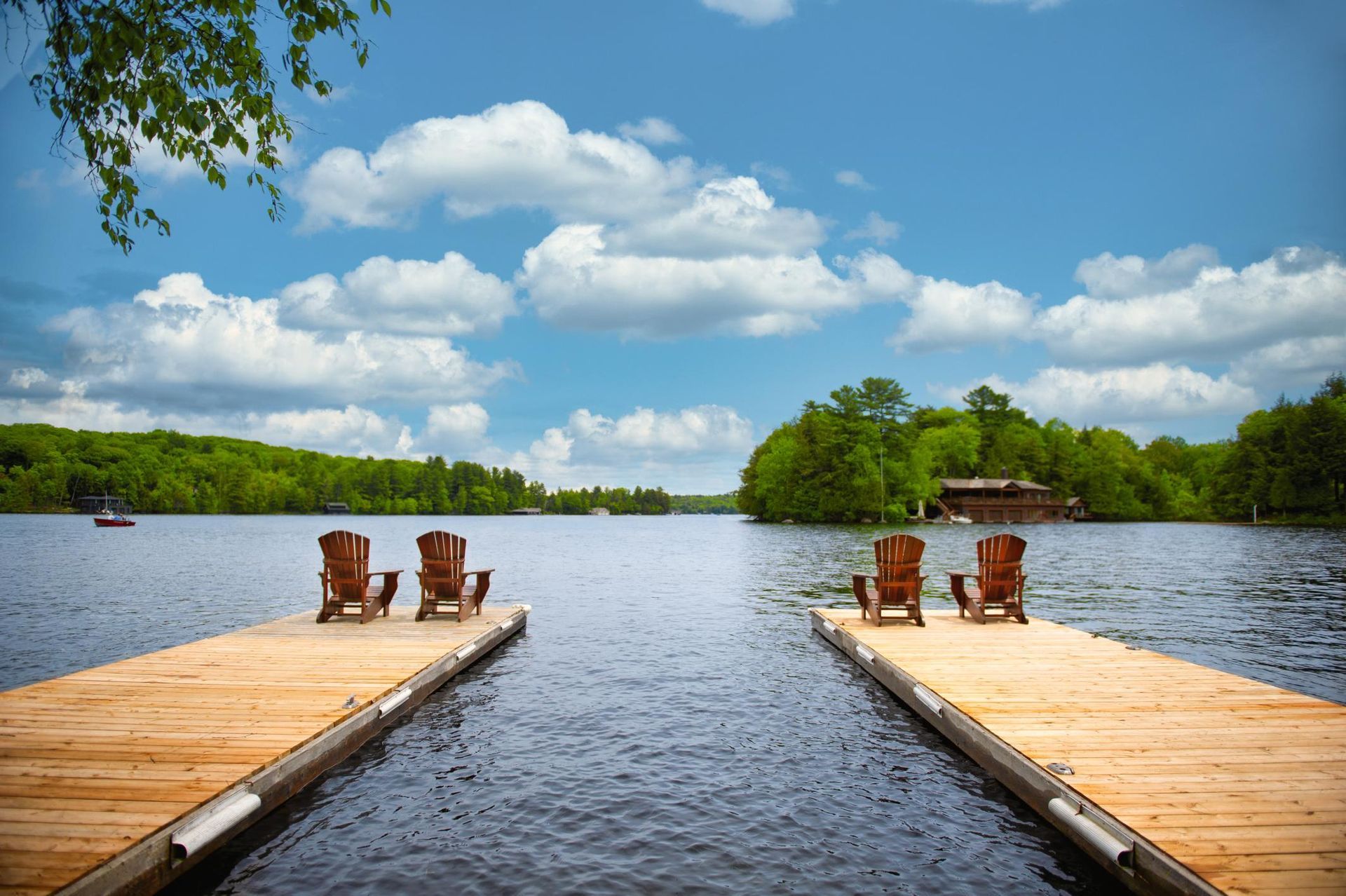 Two wooden docks with chairs on a lake under a blue sky with clouds; trees line the shore.