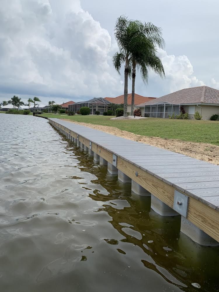Dock extending into a body of water with homes and palm trees in the background under a cloudy sky.