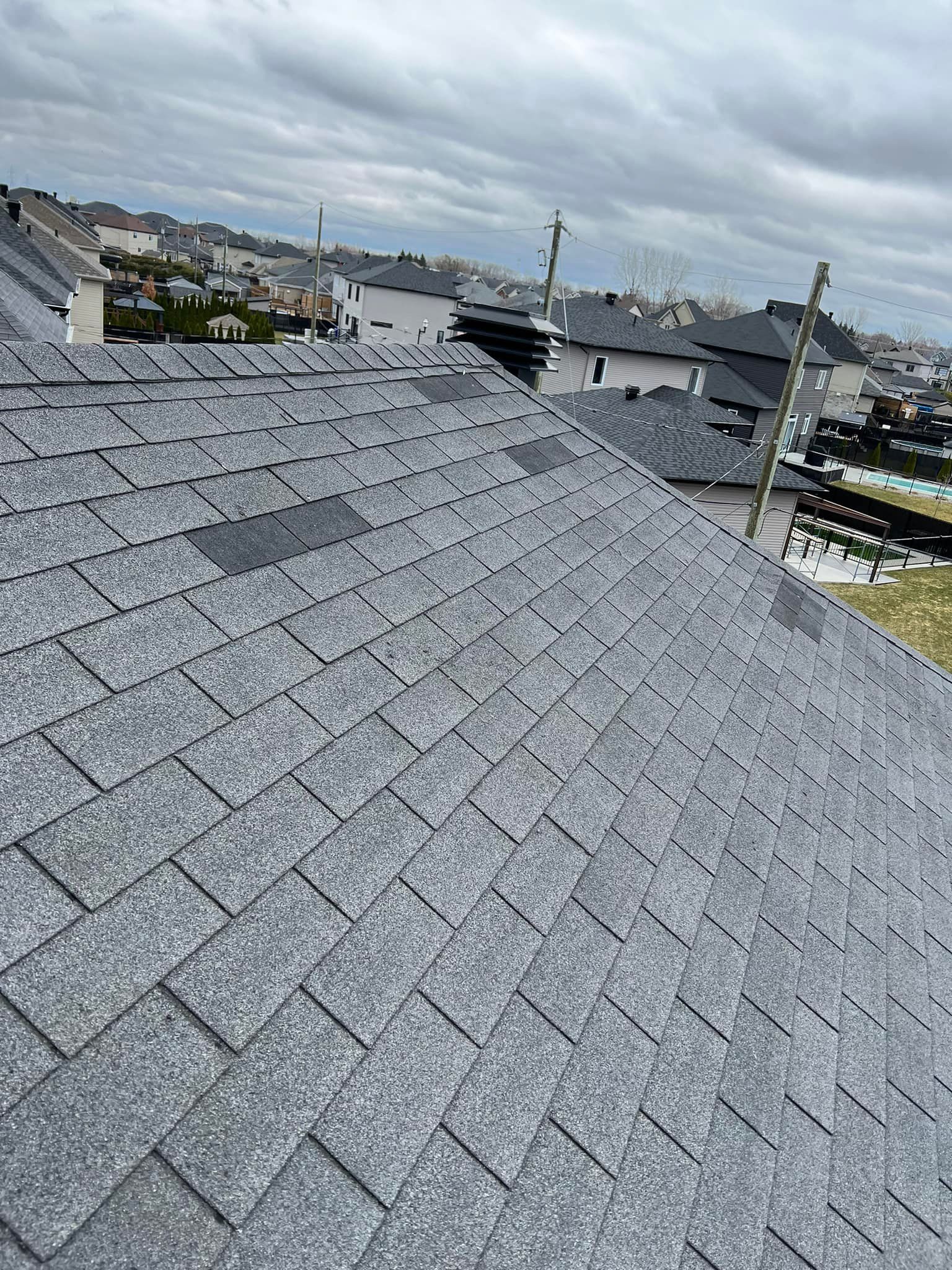 Gray shingled rooftop with a distant neighborhood skyline under a cloudy sky