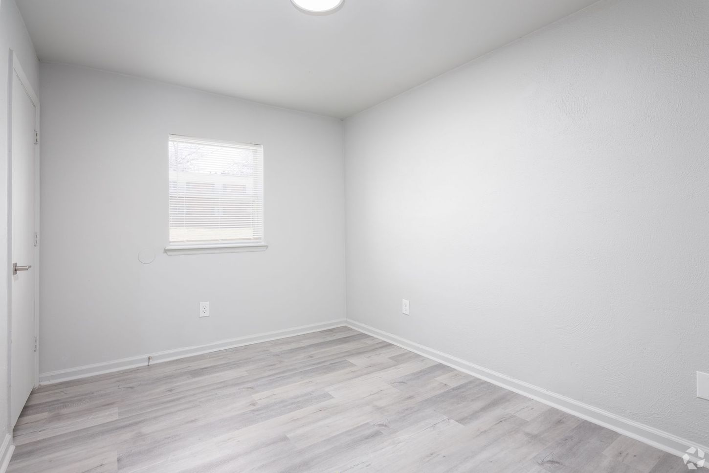 An empty bedroom with hardwood floors , white walls and a window.