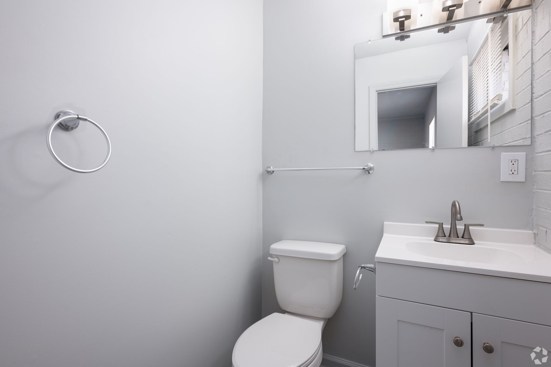 A bathroom with a toilet , sink and mirror.