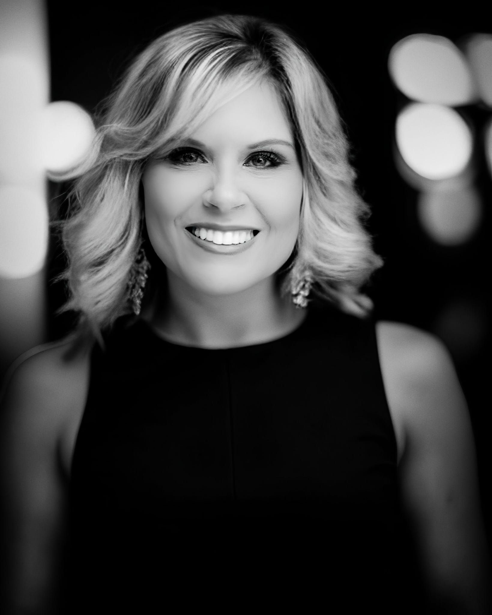 Lady Jen Du Plessis  in a black suit is sitting on a desk.