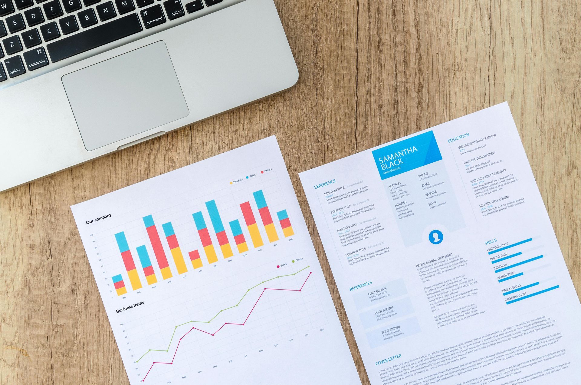 Laptop and two printed documents with charts and data on a wooden desk.