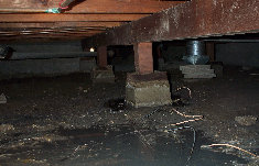 A dirty basement with a wooden floor and a brick pillar.