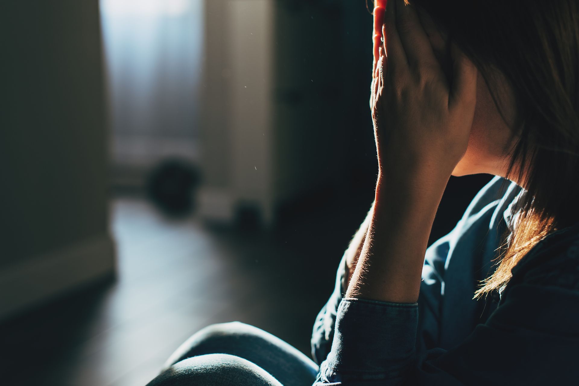 A woman is sitting on the floor covering her face with her hands.