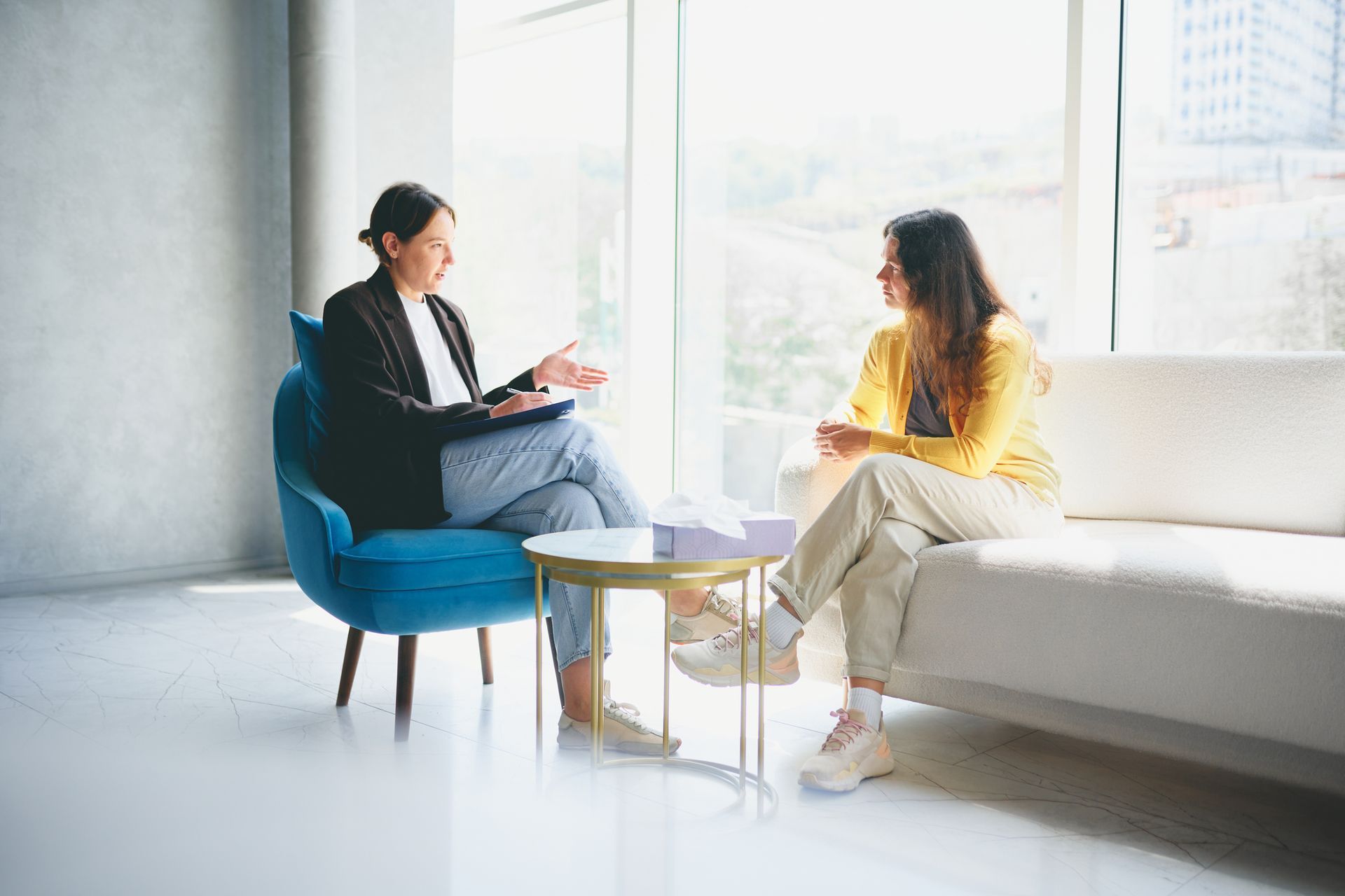 Two women are sitting on a couch talking to each other.