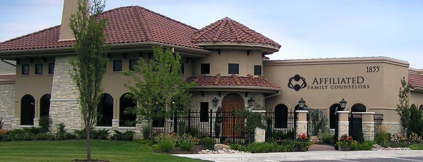 A large house with a red tile roof is surrounded by trees and bushes.