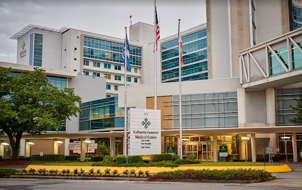 Hospital building exterior with flags and entrance; lush landscaping in front.