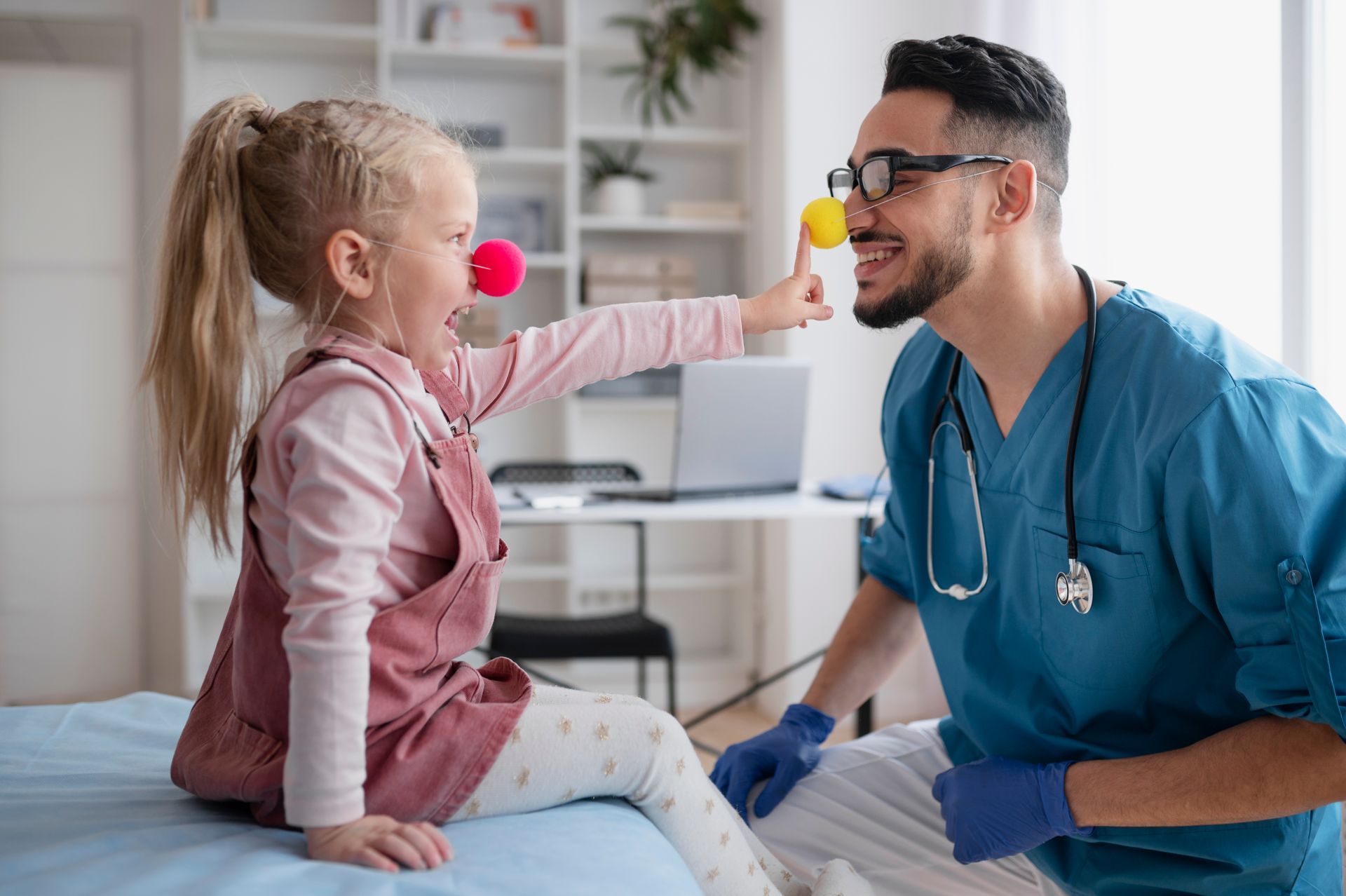 Child and doctor with red clown noses, laughing in a medical office setting.