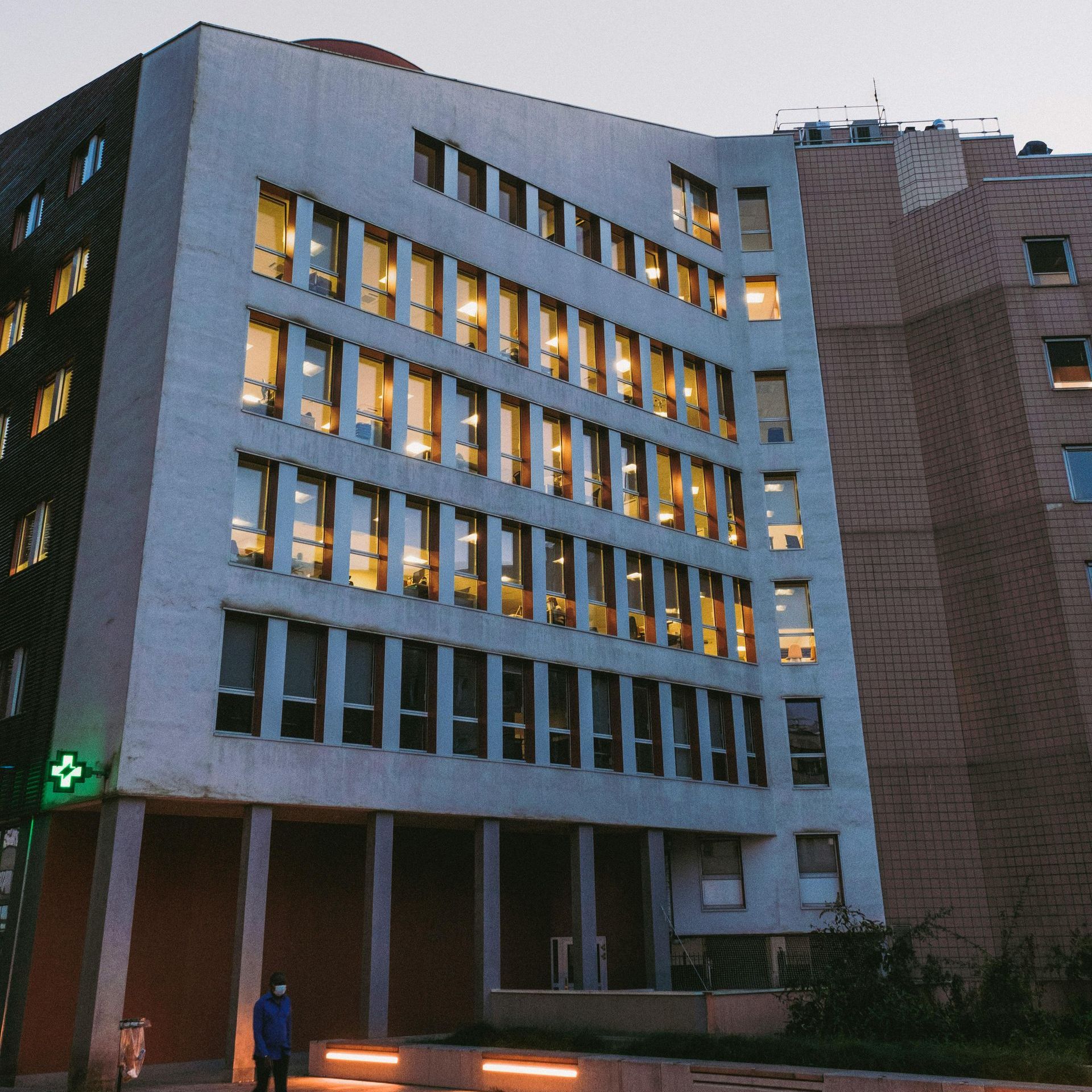 Modern office building at dusk, with lit windows and a person standing below.