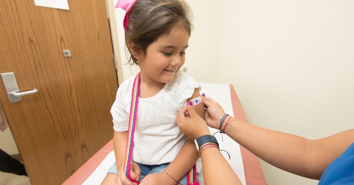 Young girl smiles while a healthcare worker prepares her for a shot in an exam room.