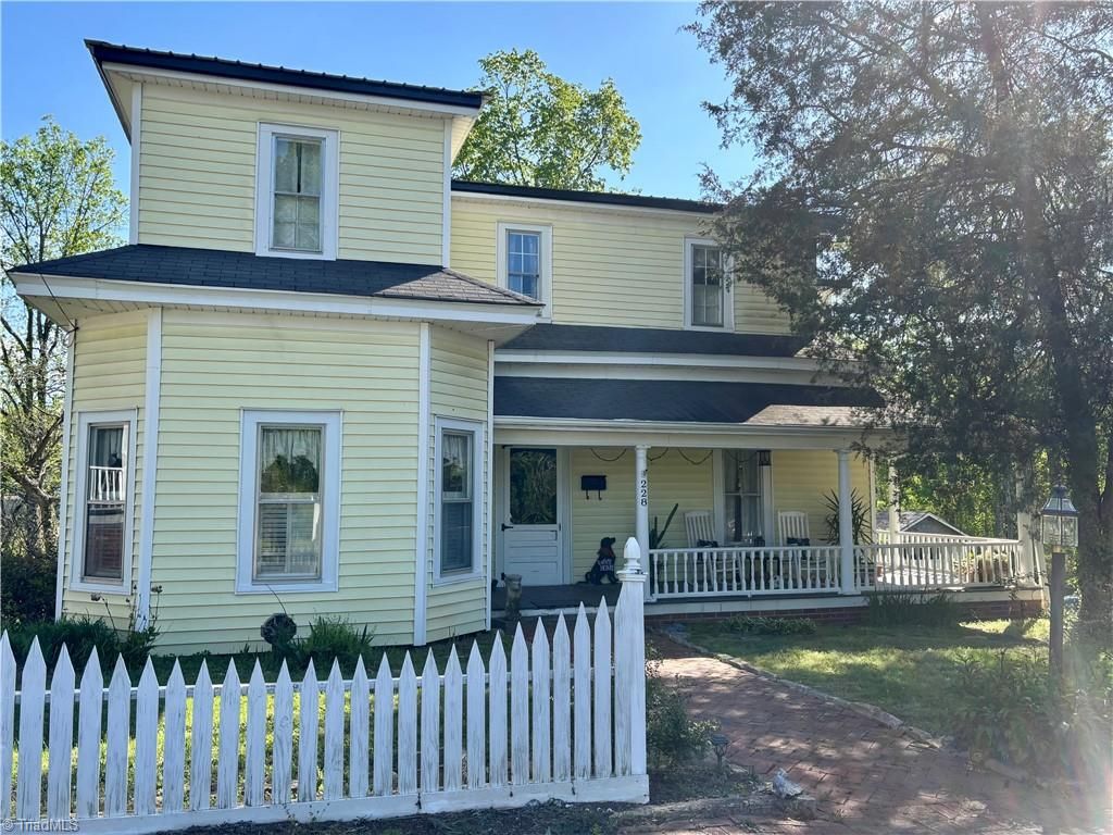 Yellow two-story house with white picket fence, porch, and trees against a blue sky.Celeste Snow, Golden Key Realty Elkin NC