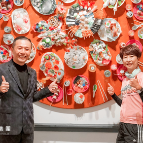 兩個人面帶微笑，豎起大拇指站在一個圓形橙色展示架前，展示架上擺放著各種白色陶瓷盤。