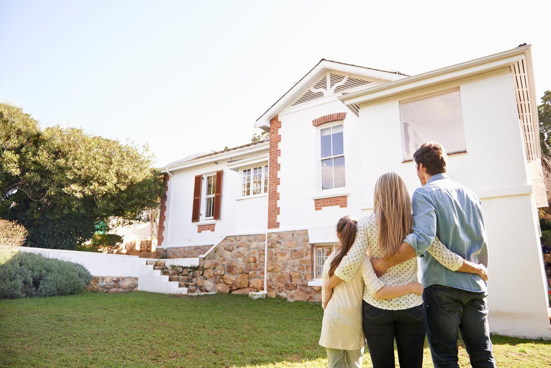 A family is standing in front of a house looking at it.