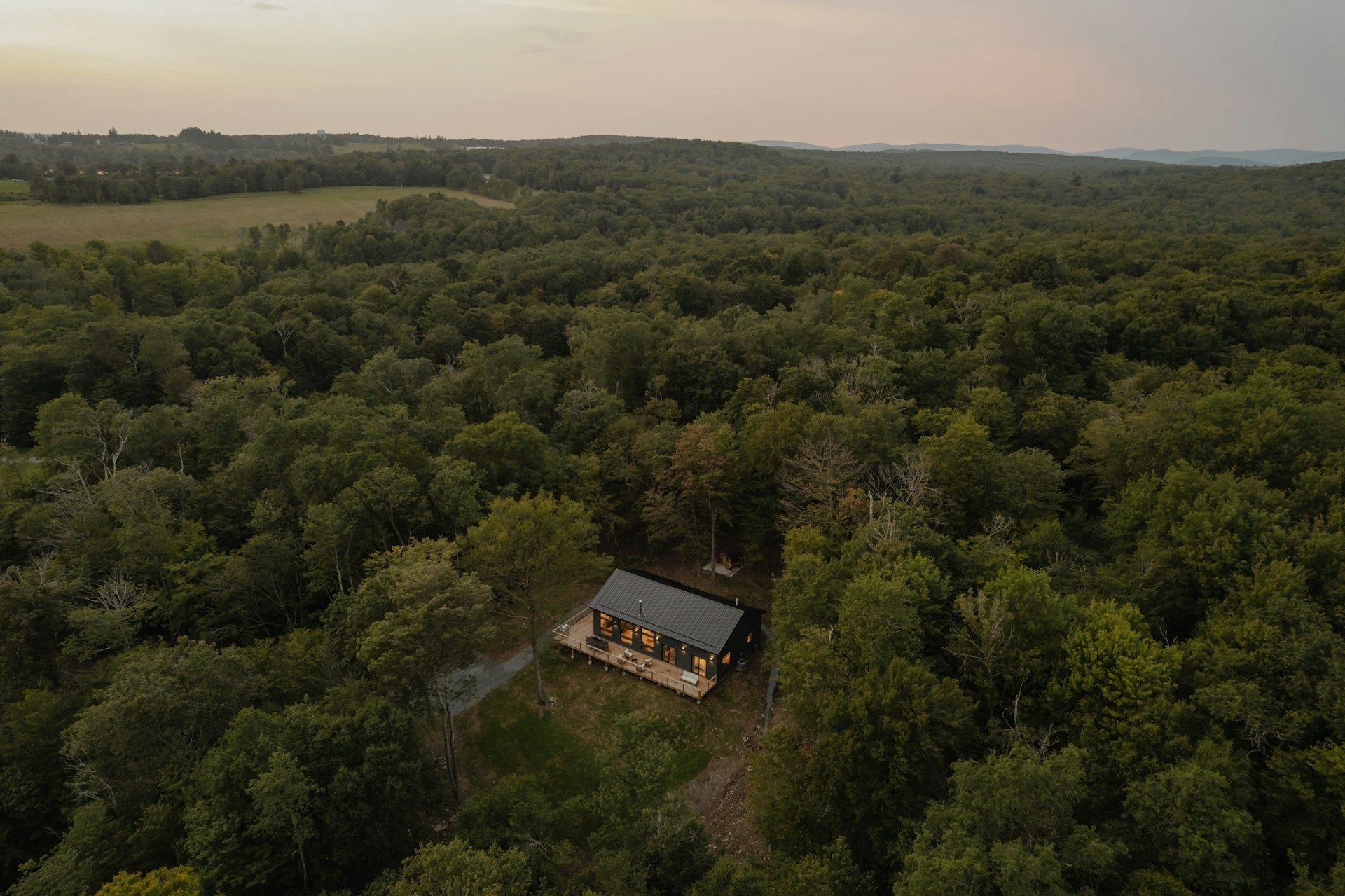 A large house with a porch is surrounded by trees in a field.