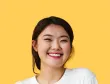 A woman in a white shirt is smiling with a yellow background.
