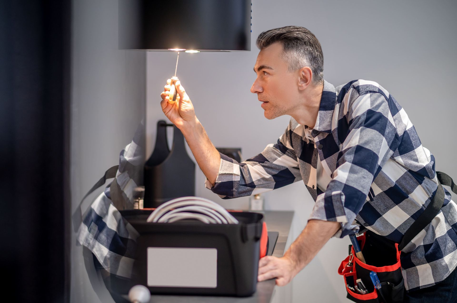 Man in plaid shirt, fixing light fixture with screwdriver, tools in a toolbox.