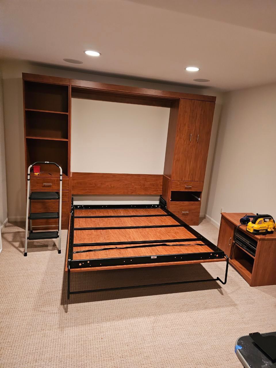 Wall bed frame in open position with attached bookshelves and a bedside table.