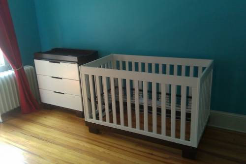 Child's room with crib, shelf decor, cube storage with woven baskets, and a wooden dollhouse.