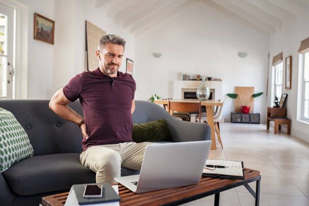 Man stretching on a sofa in a bright living room with a laptop on the coffee table