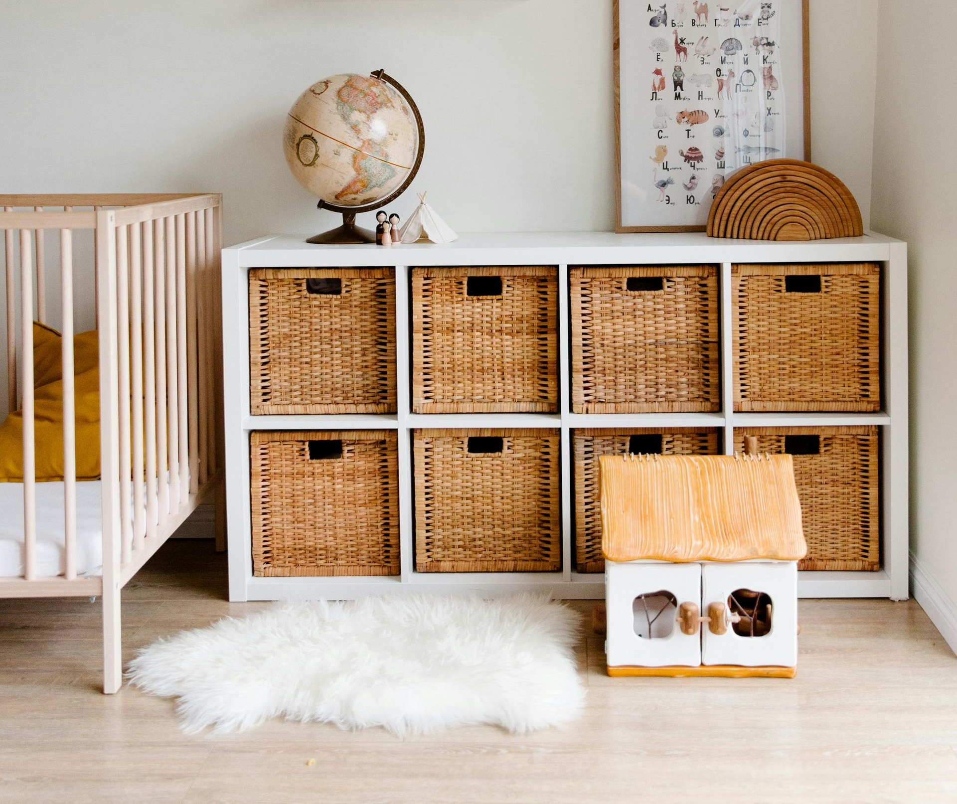 Child's room with crib, shelf decor, cube storage with woven baskets, and a wooden dollhouse.