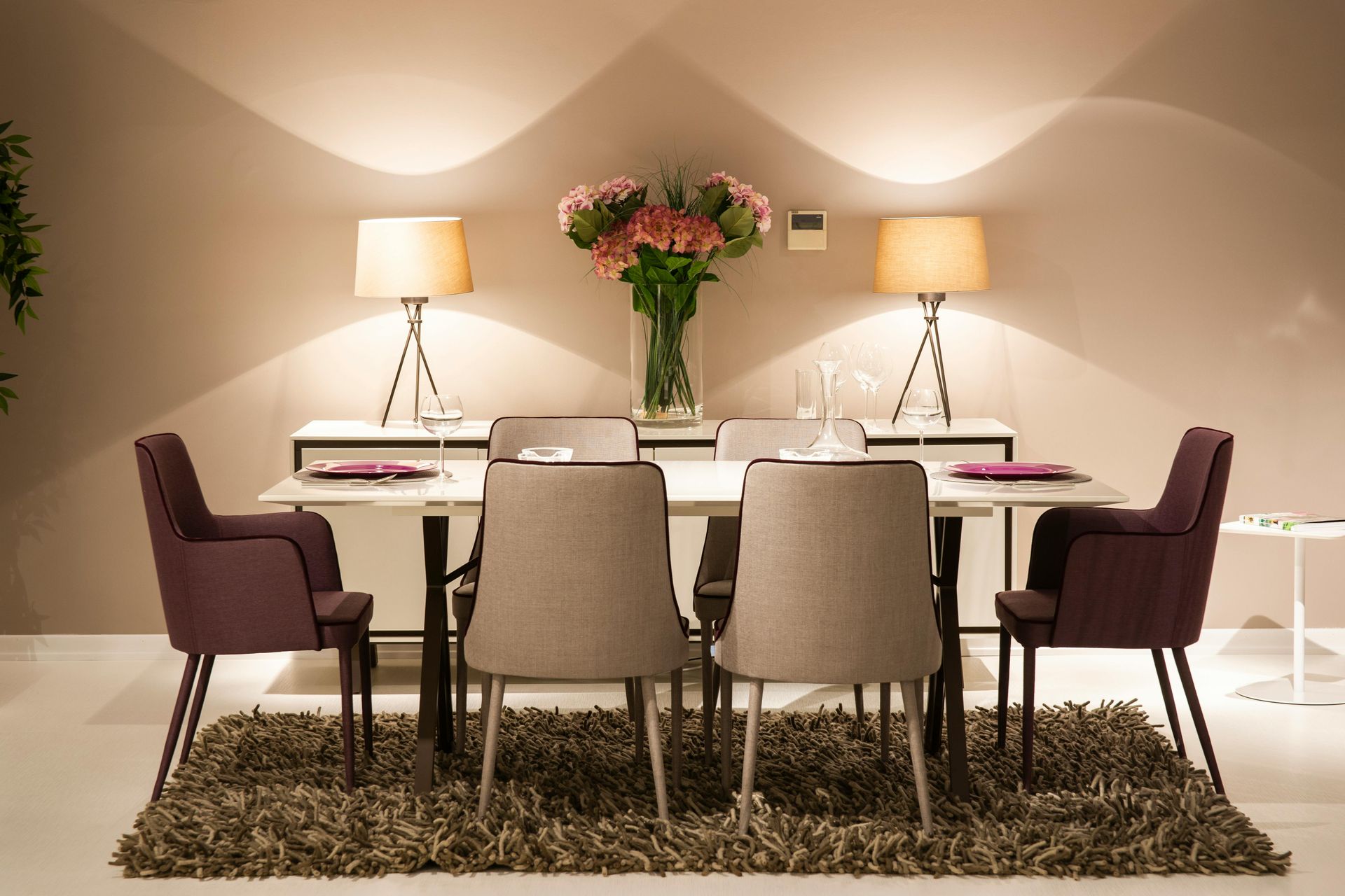 Elegant dining room with a set table, flower centerpiece, lamps, and six chairs on a shag rug